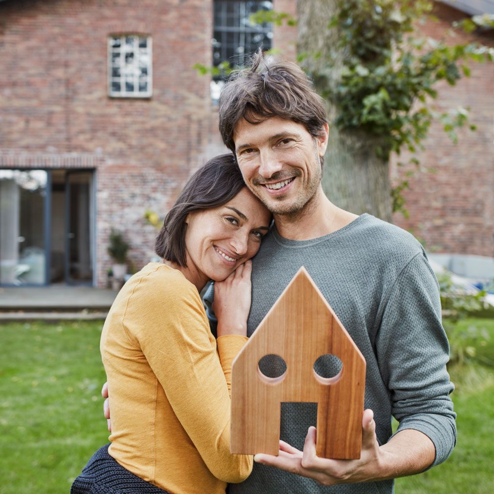 Glückliches Paar hält ein Hausmodell vor einem Wohnhaus