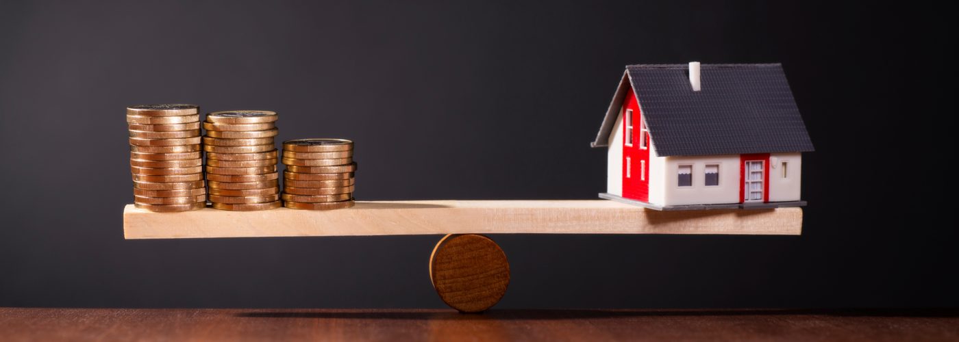 Hausmodell und Münzstapel auf einer Waage als Symbol für Baufinanzierung