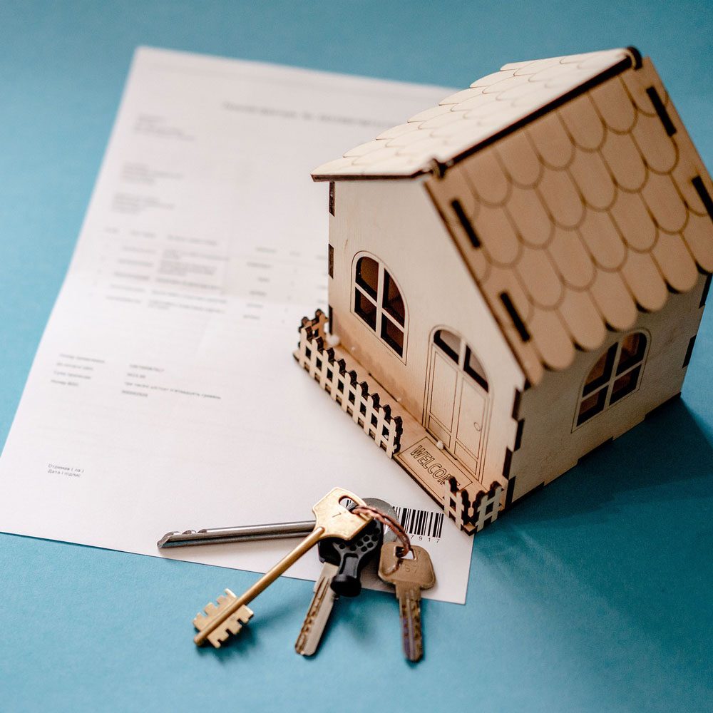 Modellhaus aus Holz mit Schlüsseln und Kaufvertrag