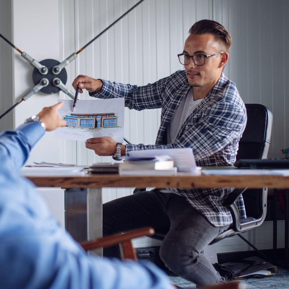 Immobilienberater erklärt Bauzeichnung im Beratungsgespräch